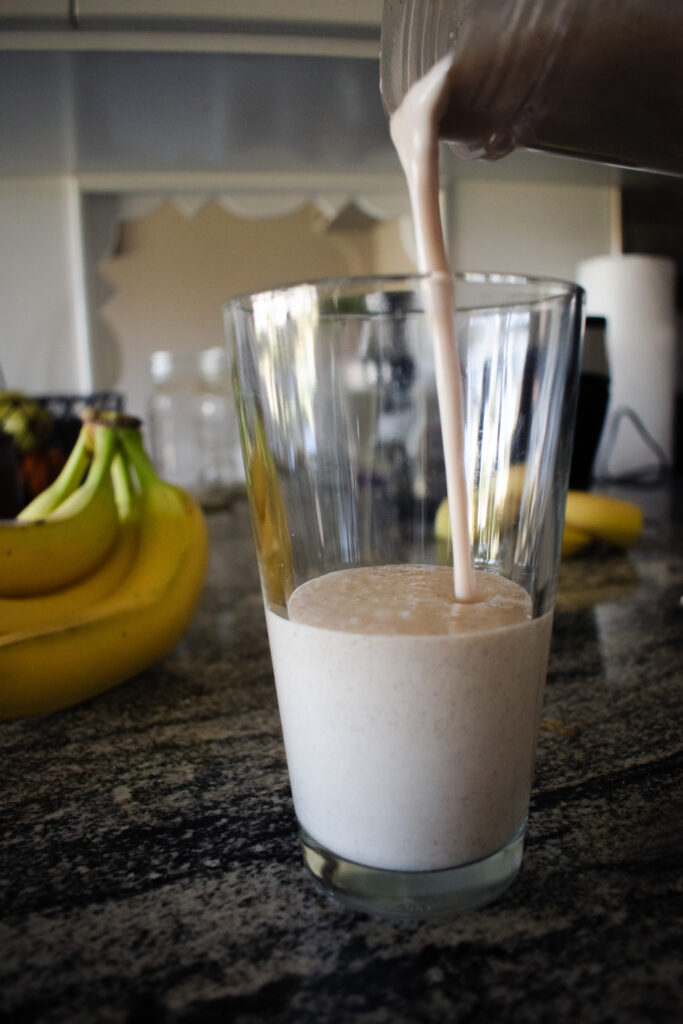 pouring a protein shake into a glass with bananas in the background