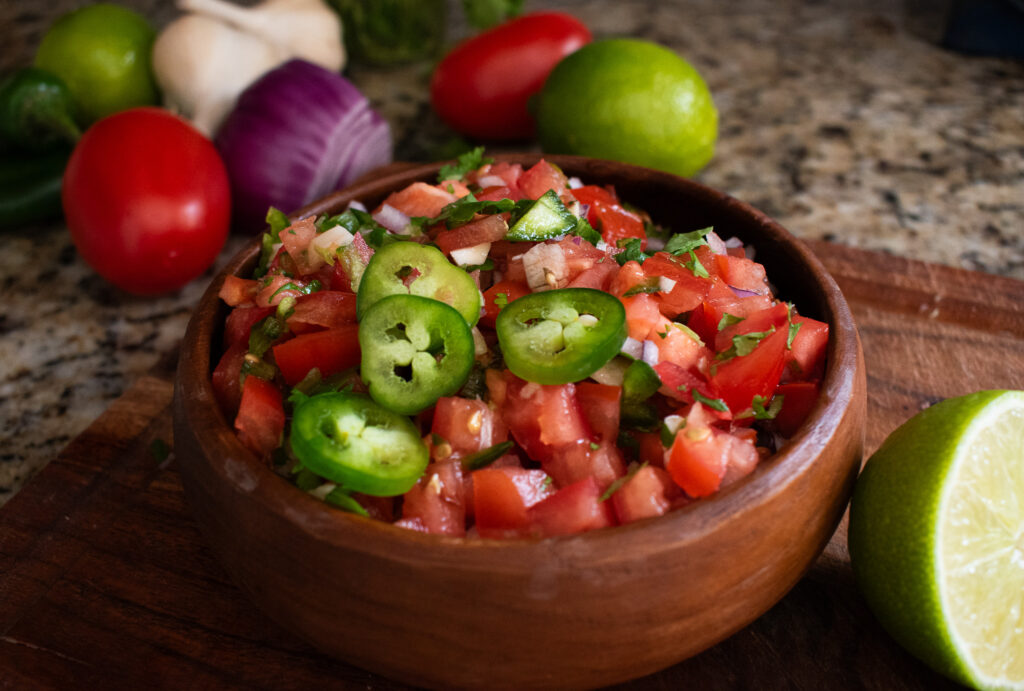 wooden bowl of pico de Gallo with ingredients around it 