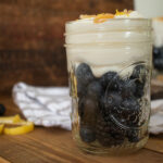 side shot of a mason jar with blue berries topped with greek yogurt and crystalized ginger