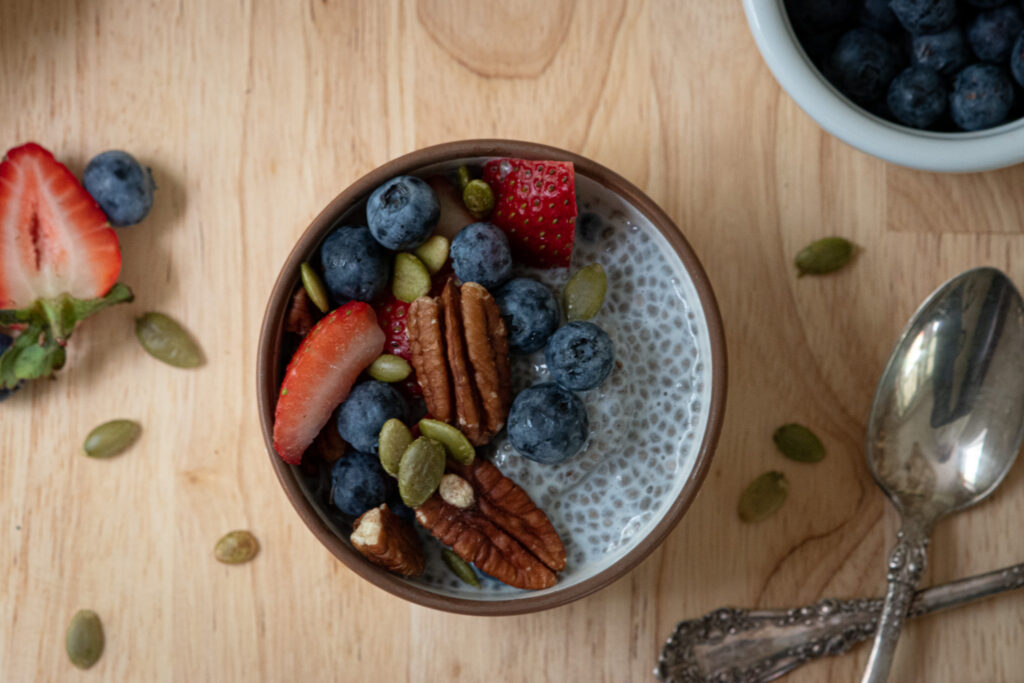 overhead shot of chia seed protein pudding with fresh berries on it and spoons beside