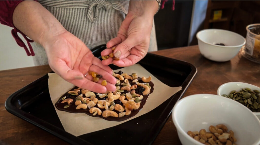 hands holding golden raisins while making a chocolate bark
